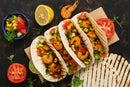 Three grilled tortillas filled with seasoned shrimp, avocado, corn, and tomato are arranged on a board. Served with SALTOPIA Infused Sea Salts Saltopia Mexican Food Lovers Set - TACO'CLOCK for vibrant flavor, plus fresh salsa, citrus, and herbs.