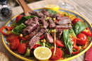 A vibrant salad topped with grilled steak rubbed in SALTOPIA’s TACO'CLOCK Mexican Food Lovers sea salt, cherry tomatoes, corn, spinach, and bell peppers, garnished with lemon halves and served on a decorative plate with a wooden spoon.