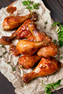 Seven glazed chicken drumsticks, seasoned with SALTOPIA Infused Sea Salts' Thrills for the Grill, are arranged on parchment paper and garnished with parsley and thyme, ready to impress at your next barbecue.