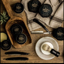 Immaculate Dense Shave Soap For Smooth Men Wet Shaving by The Immaculate Beard—alongside tins, a brush, razors, scissors, and a comb—arranged on a rustic wooden surface with towels and a small plant; the perfect setup for those who appreciate a traditional wet shaving experience.