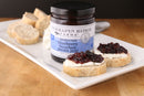 Terrapin Ridge Farms Blueberry Bourbon Pecan Jam Quart is shown on a plate with sliced baguette and cheese—ideal for charcuterie boards. Two baguette slices are topped with the gourmet jam, while extra bread sits in the background.