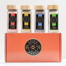 Discover the Spice Wheel Mocktail Sugar Gift Set: four glass jars of flavored sugars—strawberry, lemon, blueberry, and lime—each topped with a wooden lid and elegantly arranged on an orange Spice Wheel box featuring the bold black and gold logo. Perfect for tea, baking, mocktails, or cocktails, this gourmet gift set from Spice Wheel adds a touch of sweetness to any occasion.