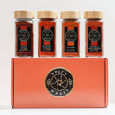 Four spice jars labeled Aleppo Pepper, Kashmiri Powder, Cayenne, and Guajillo Chili Powder are arranged on top of an orange Spice Wheel box featuring a circular logo at its center—this is the Spice Wheel Fiery Four Gift Set – A Global Heat Collection by Spice Wheel, a vibrant chili powder assortment that makes the perfect spice gift set for adventurous cooks.