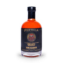 A 6 oz glass bottle of Spicewalla T-Pain x Spicewalla - The Sauce (Perfectly Imperfect Edition) hot sauce, featuring a striking black label with an illustrated face sporting sunglasses and bold gold “T-PAIN THE SAUCE” text. This edition delivers a punchy sweet and smoky flavor, with its vibrant orange-red hot sauce that pops both in taste and on your shelf.