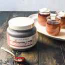 A quart jar of Terrapin Ridge Farms Raspberry Amaretto Jam sits on a wooden table beside a spoonful of jam and three chocolate mousse desserts topped with whipped cream on a white tray.