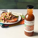 A bottle of Terrapin Ridge Farms Garlic & Herb Vinaigrette sits on the counter, with toast topped with white beans and vegetables behind it. A fork rests on the plate.