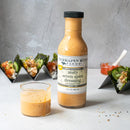 A bottle of Terrapin Ridge Farms Zesty Seven Spice Dressing stands next to a glass of the dressing, with sushi hand rolls in the background and a small dish of pickled ginger on a light gray surface.