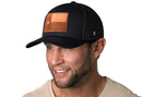 Smiling man with short brown hair and beard wearing a Haka Hat Texas Flag Trucker Hat Leather (Black Texas Flag Snapback) and a light beige shirt, shown against a white background.