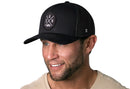A man wearing a black Haka Hat San Antonio Trucker Hat, the SAN X Snapback, with a circular patch featuring S, A, N letters and an H logo.