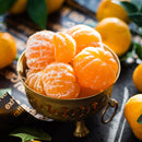 A brass bowl filled with several peeled tangerines sits on a table, surrounded by whole, unpeeled tangerines and green leaves in natural light—a scene evocative of the sunlit orchards that inspire Georgetown Olive Oil Co. Tangerine Balsamic Vinegar, crafted by Georgetown Olive Oil Co. with the same artisanal care and attention to detail.