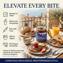 A jar of Taycte Taycte Organic Hazelnut Cocoa Cream by Taycte rests on a table alongside toast, pastries, and orange juice, with a view of a Mediterranean coastal town in the background. Icons highlight delicious ways to enjoy the spread, including on toast and stirred into yogurt.