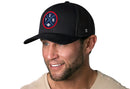 A man with a short beard and light eyes smiles while wearing the Haka Hat Tennessee Trucker Hat | Black TEN X Football Snapback by Haka Hat and a beige T-shirt against a plain white background.
