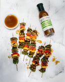 Colorful vegetable skewers with bell peppers, onions, and mushrooms are arranged on marble near a bowl of sauce and a bottle of Terrapin Ridge Farms Ginger, Miso and Honey Salad Dressing, with some drips on the surface.