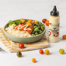 A bowl with white rice, greens, cherry tomatoes, cucumber slices, and Terrapin Ridge Farms Horseradish Sauce Squeeze sits on a yellow striped cloth. Nearby are a bottle of Terrapin Ridge Farms sauce and assorted cherry tomatoes.