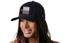 A woman with long brown hair wears a Haka Hat Texas Flag Trucker Hat (Black TX Snapback) by Haka Hat, featuring a black, gray, and white flag patch with a star. She smiles and looks to the side against a white background.