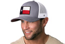 A man smiles and looks to the side while wearing a Haka Hat Texas Flag Trucker Hat | Gray-White TX Snapback by Haka Hat, featuring a front patch, against a white background.