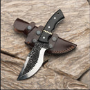 The Texan Knives Tom Brown Tracker Survival Knife, featuring a D2 steel blade and a brass & buffalo horn handle, rests on a brown leather sheath atop a textured wooden surface.
