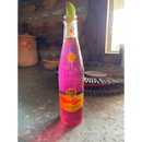 A glass bottle of Topo Chico is filled with a vibrant pink Prickly Pear Margarita made using Brushfire Farms Bulk Prickly Pear Simple Syrup, topped with a lime wedge and chili powder, and sits on a rustic countertop near a sunlit window.