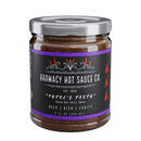 A 9oz jar of Harmacy Hot Sauce Co. Totec’s Teeth Extra Hot Pasilla & Plum Sauce, featuring a black label with red flames and purple accents, described as a deep, rich, fruity sauce made with super-hot peppers.