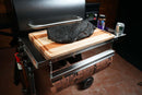 A large brisket sits on a Pimp My Grill® Tactical Stainless Folding Front Shelf atop a grill, with a roll of butcher paper hanging underneath.