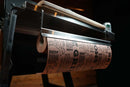 A roll of printed butcher paper hanging from a Pimp My Grill® Tactical Stainless Folding Front Shelf for Traeger Pro 22 / Pro 575 / Redland / Ironwood 650.