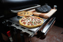 A Pimp My Grill® Tactical Stainless Folding Front Shelf attached to a Traeger Pro 780 grill, holding a pizza, a fruit pie, and a large piece of smoked meat on a cutting board.