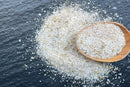 A wooden spoon rests on a pile of World Spice Tuscan Rosemary Salt, scattered across a dark textured surface—evoking the rustic flavors of Tuscany, where blends like this from World Spice are often paired with extra virgin olive oil and regional wines.