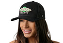 A smiling woman wears the Haka Hat Believe Trucker Hat, a black Alien UAP snapback with green UFO and BELIEVE embroidery in HAKA signature 5.0 style, set against a plain white background.