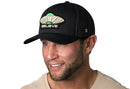 A smiling man with a trimmed beard wears the Haka Hat Believe Trucker Hat, a black Alien UAP snapback by Haka Hat with BELIEVE embroidered on the front, against a white background.