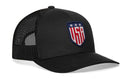 The Haka Hat USA Shield Trucker Hat is a black mesh snapback featuring a front embroidered patch with a blue shield, three white stars, and bold red USA lettering outlined in white.