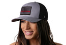 A smiling woman wears a Haka Hat Thin Red Line Trucker Hat—Gray-Black Fire Tactical Snapback with a black-and-gray American flag and fire tactical embroidered patch. The background is white.