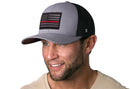 A smiling man with short brown hair and a trimmed beard wears a Haka Hat Thin Red Line Trucker Hat—Gray-Black Fire Tactical Snapback. He is dressed in a light tan shirt.