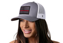 A woman wears the Haka Hat Thin Red Line Trucker Hat, a gray-white fire tactical snapback by Haka Hat, featuring a Thin Red Line American flag embroidered patch on the front.