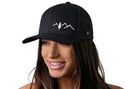 A woman with long brown hair smiles while wearing the Haka Hat Pine Tree with Mountains Trucker Hat, a black outdoors snapback by Haka Hat, featuring a white mountain and tree graphic, against a plain white background.