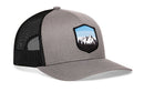 The Haka Hat Mountains and Sky Trucker Hat by Haka Hat features a gray-black design with mesh back, snapback closure, and a front patch showing mountains, trees, and a blue sky.