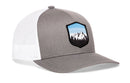 The Haka Hat Mountains and Sky Trucker Hat is a gray-white snapback featuring a mountain-and-trees patch with a blue sky, perfect for outdoor style.