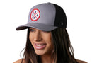 A woman smiles wearing the Haka Hat USA Trucker Hat, a gray-black snapback with a circular America patch, stars, and red accents, by Haka Hat, shown against a plain white background.