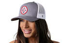 A smiling woman wears the Haka Hat USA Trucker Hat, a gray and white America snapback by Haka Hat, featuring a circular USA logo with red and black lettering and crossed lines on the front.