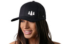 A smiling woman with long brown hair wears the Haka Hat Three Pine Trees Trucker Hat, a black outdoors snapback by Haka Hat featuring three white pine tree silhouettes on the front, shown against a plain white background.