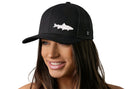 A smiling woman wears the Haka Hat Steelhead Fish Trucker Hat—a black snapback by Haka Hat with a white steelhead fish design—against a plain white background.