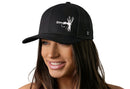 A woman with long brown hair smiles while wearing the Haka Hat Fly Fishing Trucker Hat, a black snapback from Haka Hat featuring a white fishing fly graphic on the front. The background is plain white.