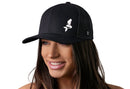 A woman with long brown hair smiles while wearing a Haka Hat Mermaid Trucker Hat in black, a comfort-fit snapback featuring a white mermaid logo on the front. The background is white.