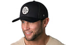 A man wears the Haka Hat PNW Trucker Hat in black, featuring a circular patch with "PNW" and a pine tree, styled in the classic Haka Hat signature snapback design.