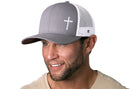 A man wearing a Haka Hat Cross Trucker Hat in gray with a white cross and white mesh back.
