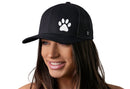 A woman with long brown hair smiles while wearing the Haka Hat Paw Trucker Hat, a black animal print snapback by Haka Hat, featuring a white paw print on the front and standing out against a clean white background.