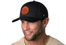 A man with a short beard and mustache smiles while wearing a Haka Hat Outdoor X Trucker Hat | Black Outdoor X Snapback with a round leather patch. He is dressed in a beige shirt, facing slightly right.