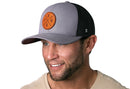 A man with a short beard, wearing a Haka Hat PNW Trucker Hat—Gray-Black PNW X Snapback—and a beige shirt, smiles against a plain white background.