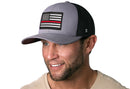 A man with a short beard is smiling and wearing the Haka Hat Thin Red Line Trucker Hat—a gray-black fire snapback by Haka Hat with a black-and-white American flag patch and a comfort-fit sweatband for all-day wear.