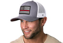 A man with light facial hair is smiling while wearing the Haka Hat Thin Red Line Trucker Hat, a gray-white fire snapback featuring a black, white, and gray American flag patch with a single thin red line.