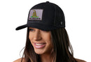 A woman smiles and faces left, wearing a Haka Hat Dont Tread On Me Trucker Hat—a black snapback by Haka Hat featuring a gray patch with a coiled yellow snake and "DONT TREAD ON ME" in Gadsden Flag Tactical style.